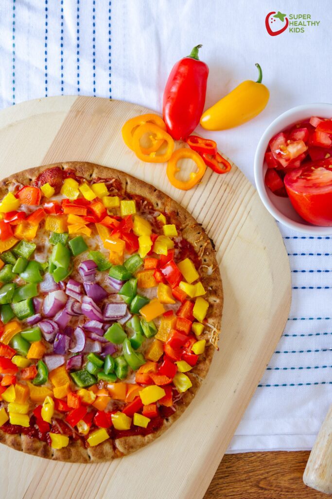 Image of bell pepper pizza kept on a wooden tray along with a bowl of chopped tomatoes
