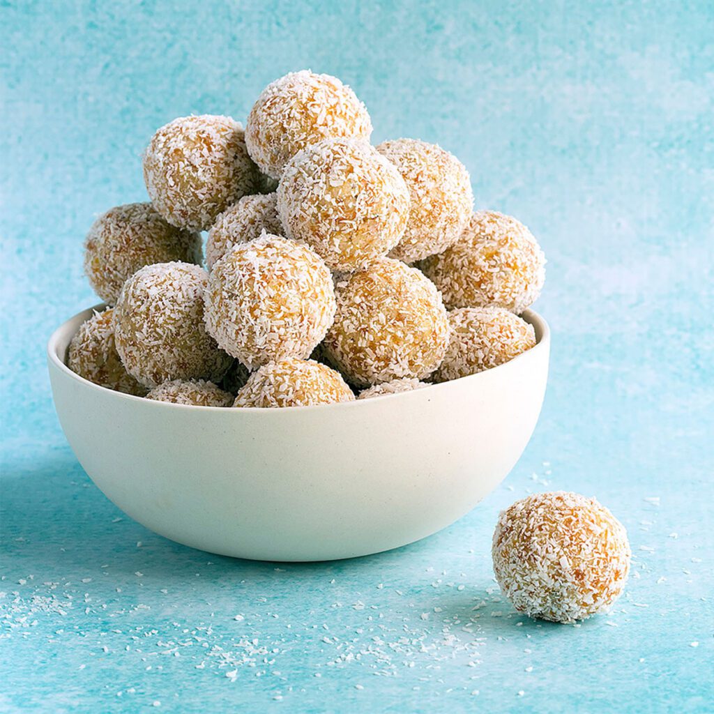 Top 10 Snacks Under 10 mins - Image of apricot balls kept in a white bowl on a blue surface