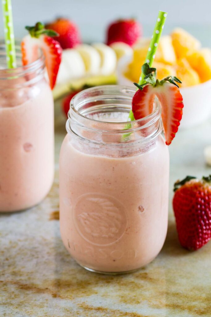 Top 10 Snacks Under 10 mins - Image of strawberry and banana smoothie served in a glass jar along with fruits kept in a plate.