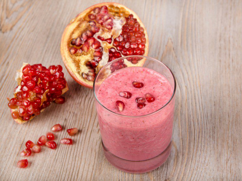 Top 10 Snacks Under 10 mins - Image of slushy pomegranate in a glass kept on a wooden table along with pomegranate kernels.