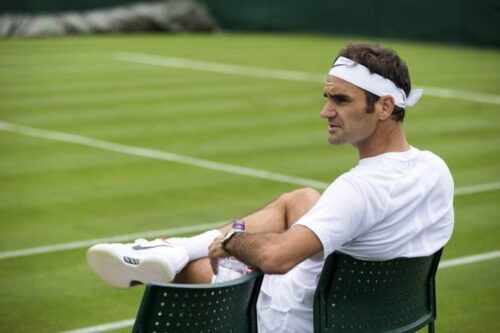 Roger Federer sitting on the sidelines of a grass tennis court
